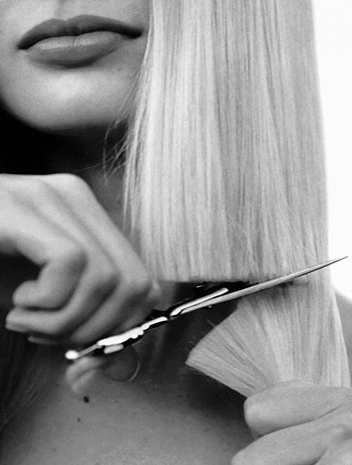 Scissors trimming blonde hair close to a person's lips