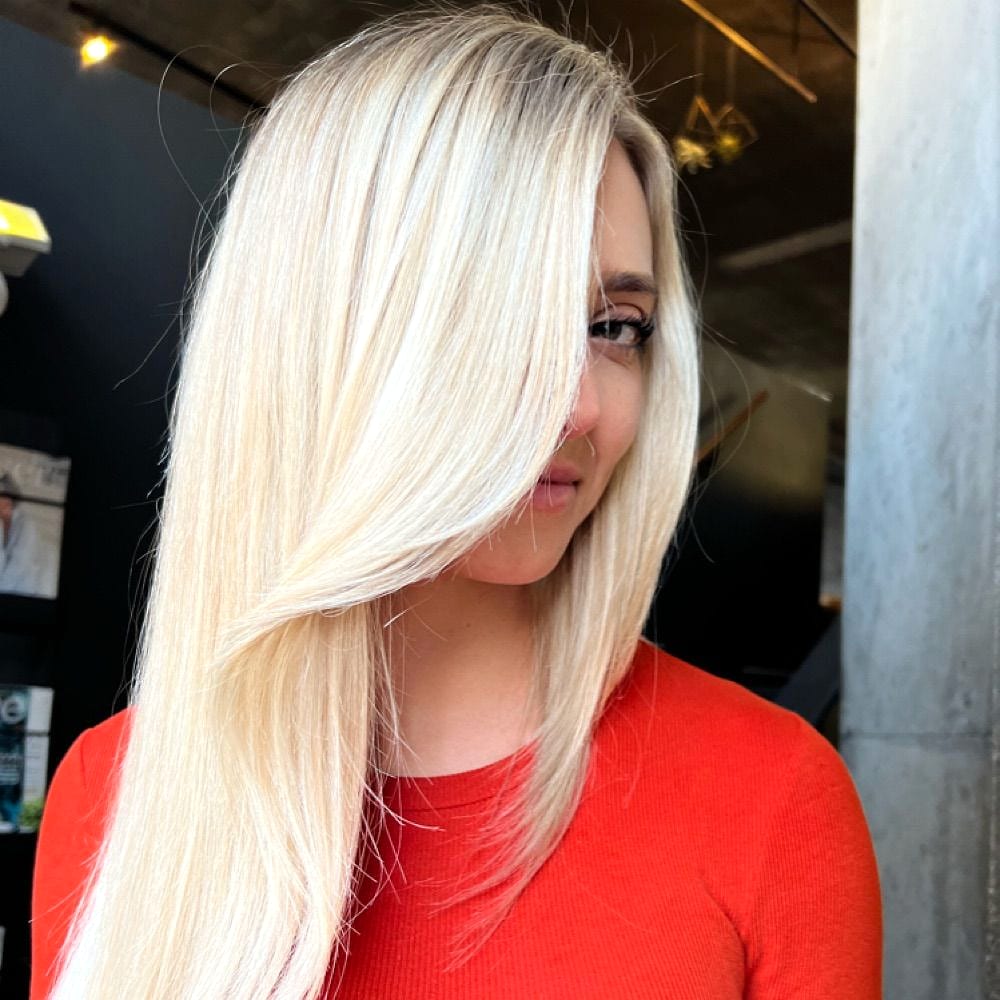 Sleek platinum blonde hair falling partly across a woman's face, worn with a red top