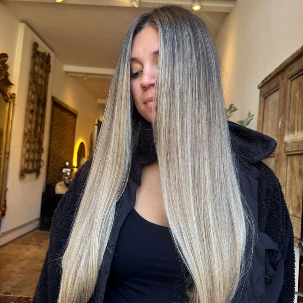 Long straight blonde and grey balayage hair on a woman looking down in a salon hallway