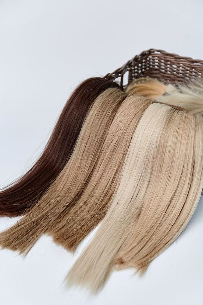 Hand-tied extension wefts lined up in shades from brown to blonde on a white background